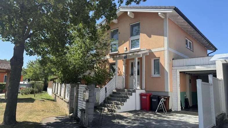 Hausfassade mit Vorgarten und Zufahrt an einem sonnigen Tag.