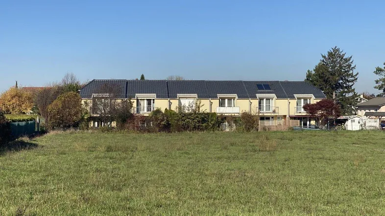 Reihenhäuser mit Balkonen und Blick auf eine weite Grünfläche unter blauem Himmel.