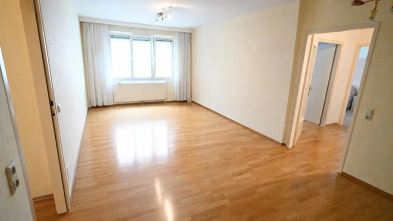 Helles, leeres Wohnzimmer mit Parkettboden und großen Fenstern, bereit zur individuellen Gestaltung.