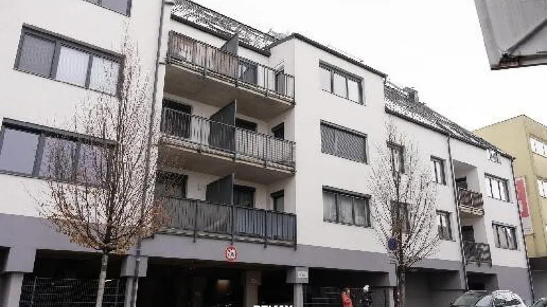 Modernes Mehrfamilienhaus mit weißer Fassade, Balkonen und dunklen Fensterläden.