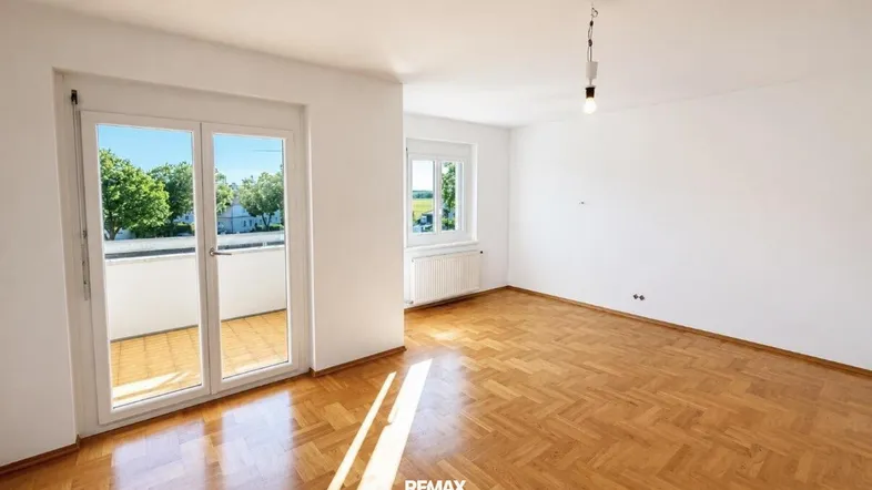Geräumiges Wohnzimmer mit hellem Fischgrätparkett und direktem Zugang zum sonnigen Balkon.