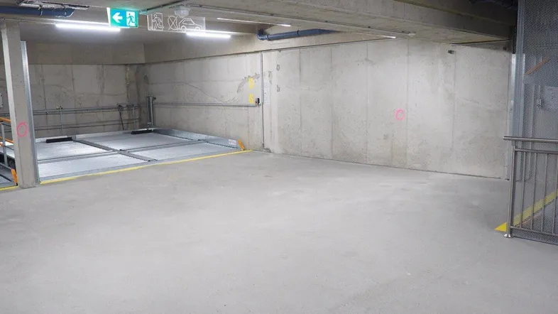 Tiefgarage mit Betonwänden und -boden, ausgestattet mit einem modernen Parkliftsystem für Fahrzeuge.