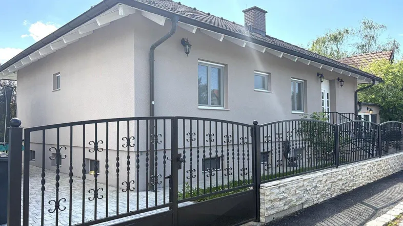 Einfamilienhaus mit gepflegter Fassade, Satteldach und schmiedeeisernem Zaun.