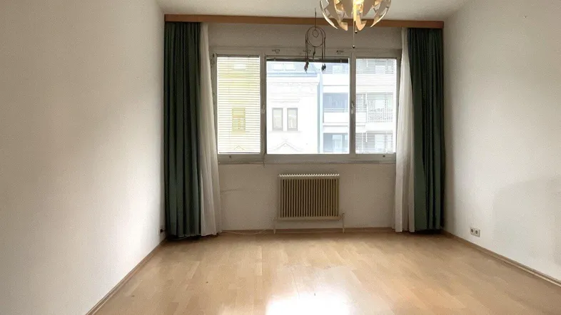 Helles Zimmer mit Parkettboden, großem Fenster und Heizkörper, bereit zur individuellen Gestaltung.