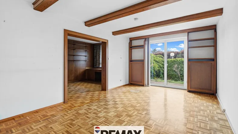 Helles Wohnzimmer mit Parkettboden, Holzbalken und Zugang zu einem weiteren Raum sowie zur Terrasse.