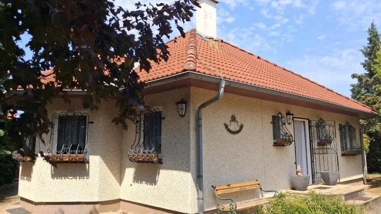 Einfamilienhaus mit rotem Ziegeldach, heller Fassade und gepflegtem Vorgarten unter blauem Himmel.