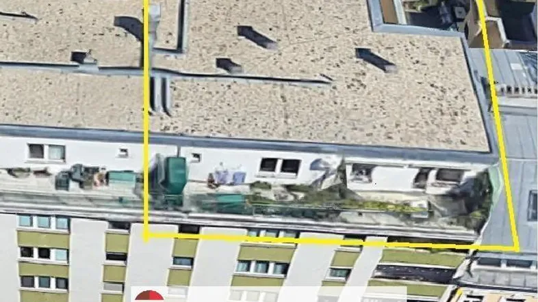 Luftaufnahme eines Gebäudes mit Flachdach und markiertem Bereich, umgeben von städtischer Bebauung.