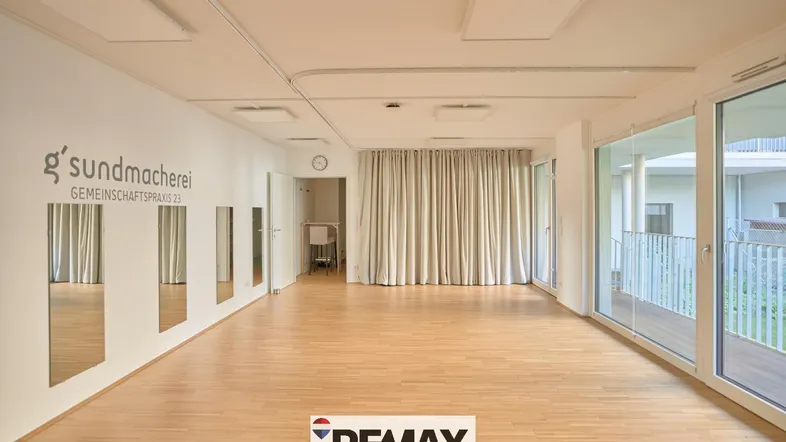Großer, heller Raum mit Holzfußboden, Spiegelfront und großen Fenstern, ideal für Kurse oder Therapien.
