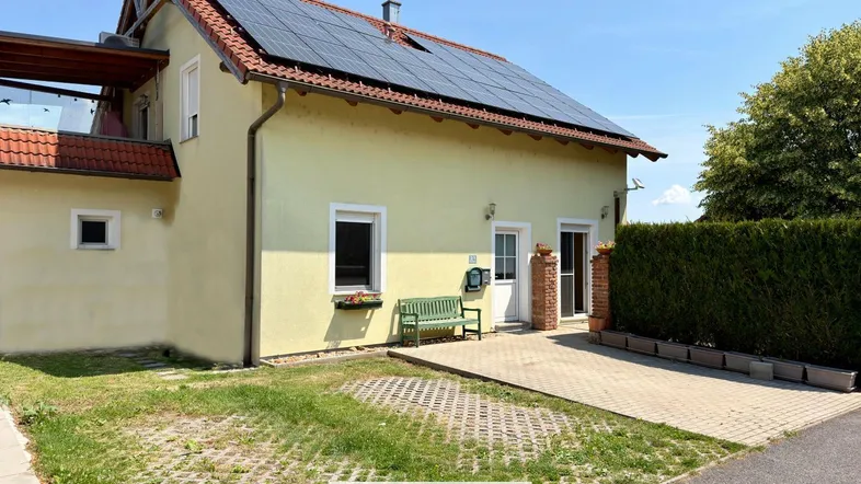 Gelbes Einfamilienhaus mit Solaranlage auf dem Dach und gepflegtem Vorgarten.