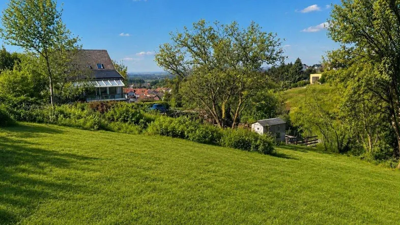 Weitläufige Grünfläche mit Blick auf ein Haus und die umliegende Landschaft unter blauem Himmel.