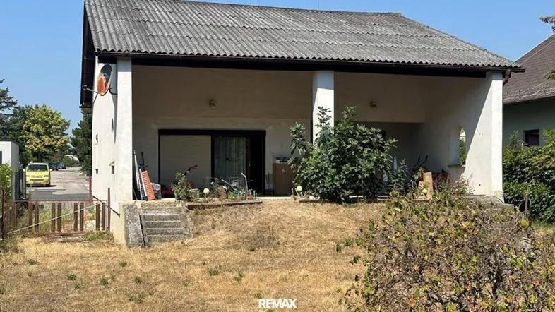 Hausfassade mit überdachtem Eingangsbereich und trockenem Garten im Vordergrund.