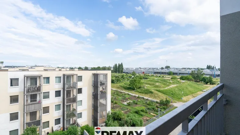Weitblick vom Balkon über grüne Flächen und benachbarte Gebäude unter einem blauen Himmel.