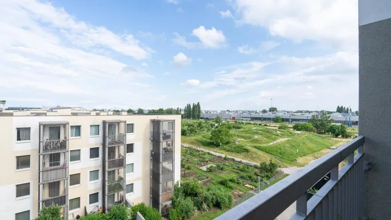 Blick vom Balkon auf eine Wohnanlage, eine Grünfläche und die weitere Umgebung unter blauem Himmel.