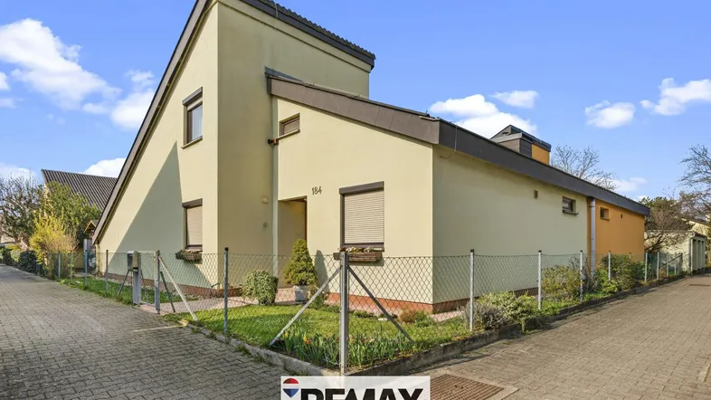 Modernes Einfamilienhaus mit heller Fassade und gepflegtem Vorgarten unter blauem Himmel.
