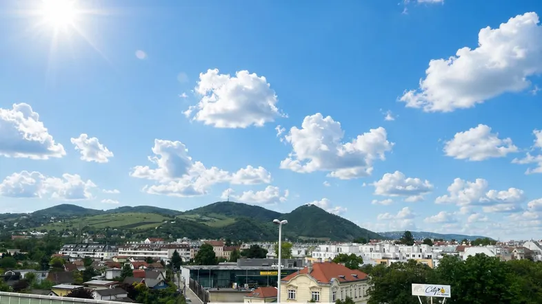Panoramablick über die Stadt mit grünen Hügeln und strahlendem Sonnenschein im Hintergrund.