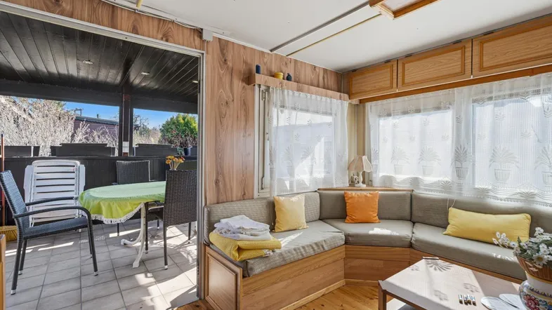 Gemütlicher Wohnbereich mit Ecksofa, Holzwänden und Zugang zu einer überdachten Terrasse.