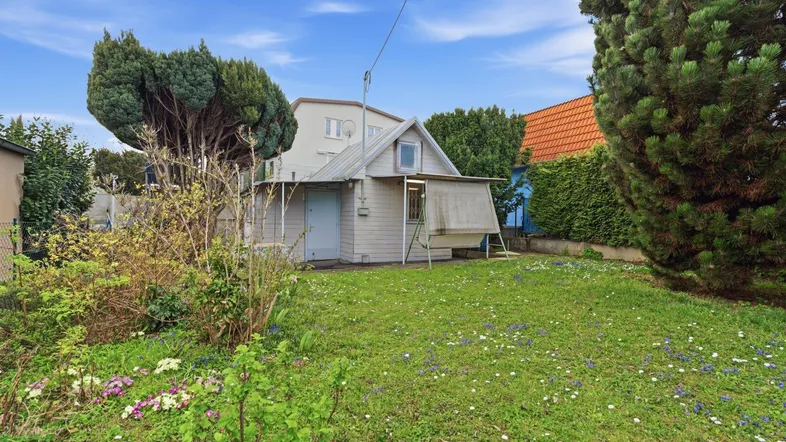 Kleines Gartenhaus mit umliegender Grünfläche und Bäumen unter blauem Himmel.