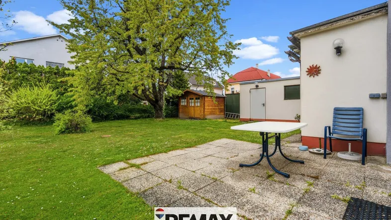 Großer Gartenbereich mit Rasenfläche, gepflasterter Terrasse und einem kleinen Gartenhaus.