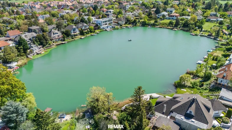 Luftaufnahme eines Sees umgeben von Wohnhäusern und viel Grün, mit einem weiten Blick über die Landschaft.