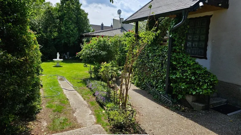 Gepflegter Gartenbereich mit Rasenfläche, Wegen und einem dekorativen Brunnen vor dem Haus.