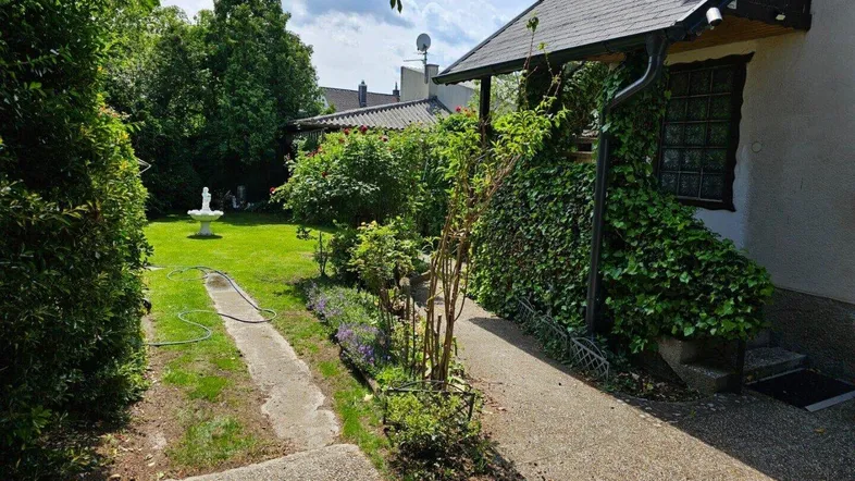 Gepflegter Gartenbereich mit Rasenfläche, Gartenweg und einem dekorativen Brunnen neben dem Haus.