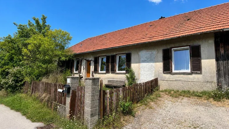 Altes Bauernhaus mit verputzter Fassade, Holzfensterläden und einem kleinen Vorgarten.