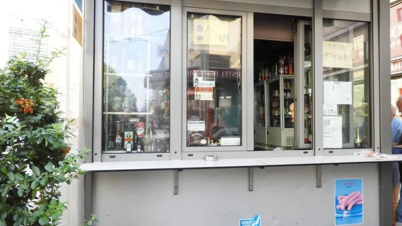 Außenansicht eines Kiosks mit großen Schiebefenstern und einer Theke zur Straße hin.