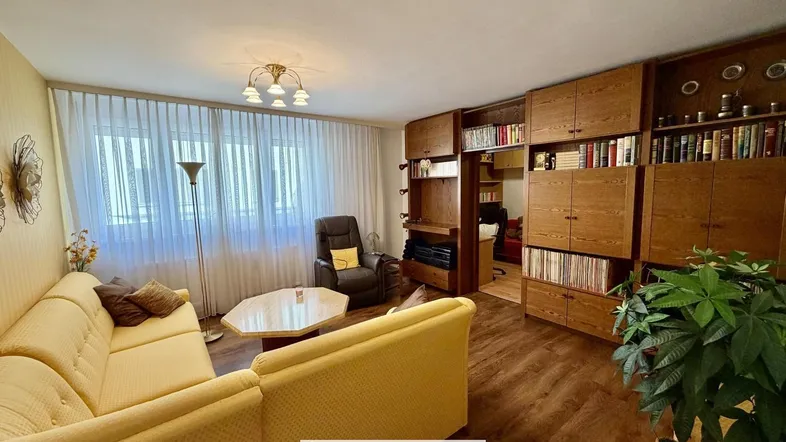 Gemütliches Wohnzimmer mit gelbem Sofa, Holzregalen und Laminatboden.