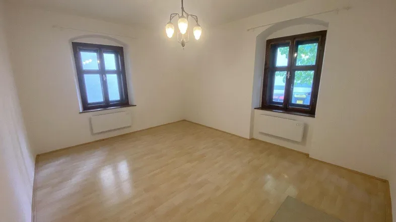 Helles Zimmer mit Parkettboden und zwei Fenstern, ideal als Wohn- oder Schlafbereich.