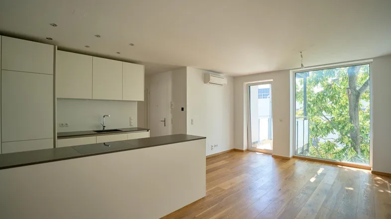 Heller offener Wohnbereich mit moderner Einbauküche, Parkettboden und Zugang zum Balkon.