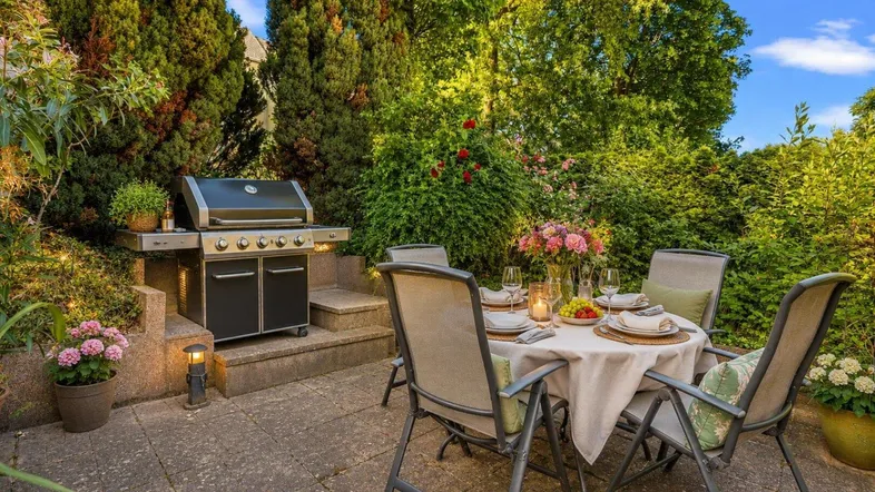 Gemütliche Terrasse mit Esstisch, Grillbereich und üppiger Bepflanzung für entspannte Stunden im Freien.