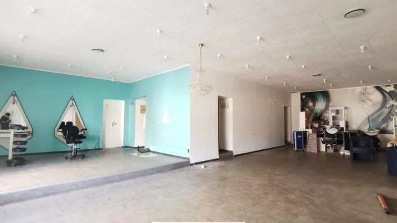 Großer Geschäftsraum mit türkisfarbener Akzentwand, Kronleuchter und Arbeitsplätzen für einen Salon.