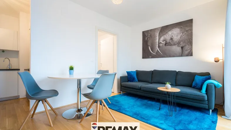 Heller Wohn- und Essbereich mit modernem Sofa, Esstisch und integrierter Küchenzeile.