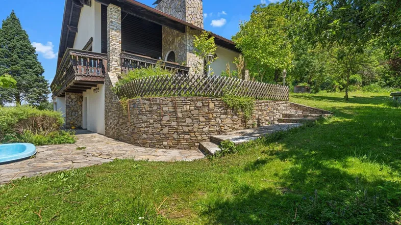 Charmantes Haus mit Steinfassade, Balkon und einem kleinen Pool im grünen Gartenbereich.