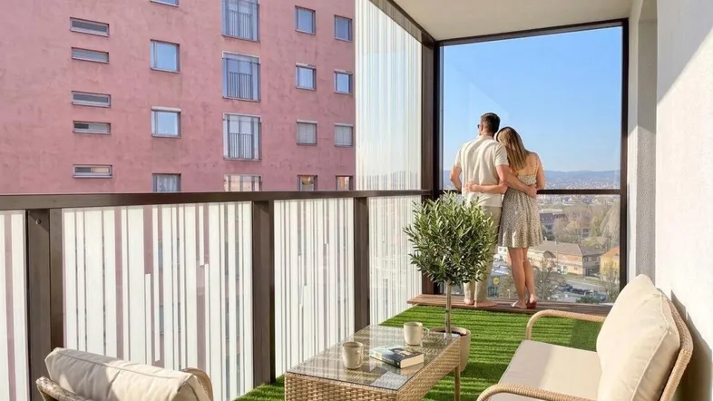 Ein Paar genießt den Ausblick von einem möblierten Balkon mit Kunstrasen und Stadtblick.