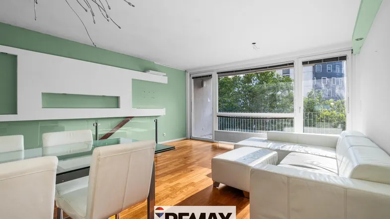 Helles Wohn- und Esszimmer mit Holzboden, weißem Sofa und Zugang zum Balkon.
