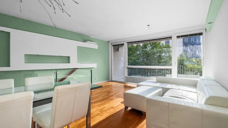 Helles Wohn-Esszimmer mit Parkettboden, weißem Sofa und Zugang zum Balkon.