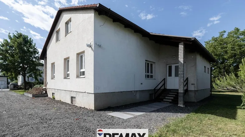 Einfamilienhaus mit heller Fassade und Kiesauffahrt unter blauem Himmel.