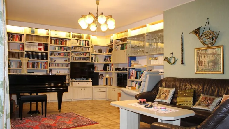 Geräumiges Wohnzimmer mit Ledersofa, Bücherregalen und einem Flügel, ideal für Musikliebhaber.