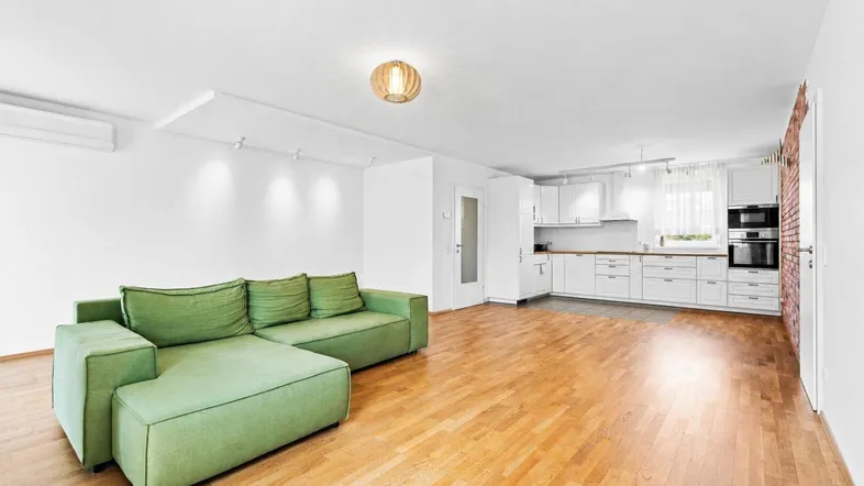 Helles, offenes Wohnzimmer mit grüner Couch und integrierter weißer Küche, ideal für modernes Wohnen.