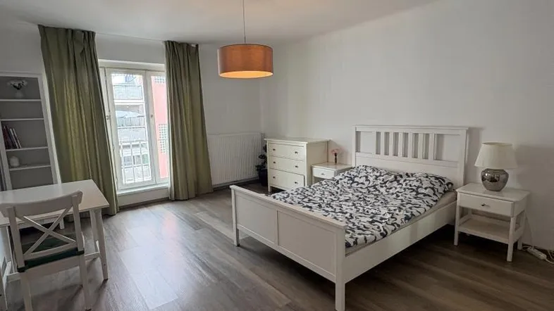 Helles Schlafzimmer mit Doppelbett, Schreibtisch und Laminatboden, ideal für Studenten oder Singles.