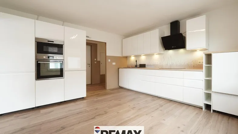Moderne Einbauküche mit weißen Hochglanzfronten, integrierten Geräten und hellem Holzfußboden.