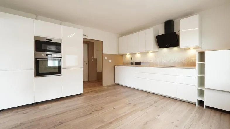 Moderne Einbauküche mit weißen Hochglanzfronten, integrierten Geräten und hellem Holzfußboden.