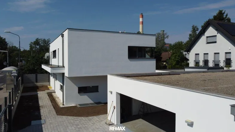 Moderne weiße Villa mit Flachdach und integrierter Garage unter blauem Himmel.