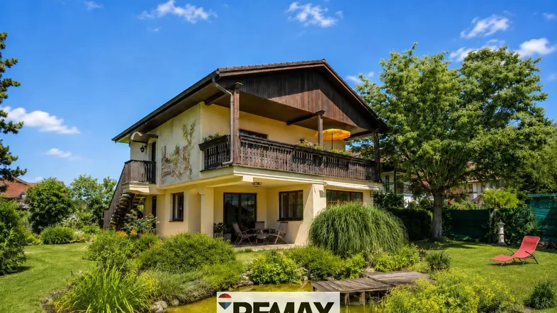 Charmantes Haus mit gepflegtem Garten, Teich und gemütlicher Terrasse unter blauem Himmel.