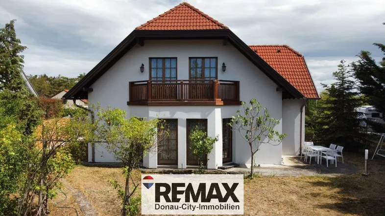 Freistehendes Einfamilienhaus mit Satteldach, Balkon und Gartenbereich unter bewölktem Himmel.