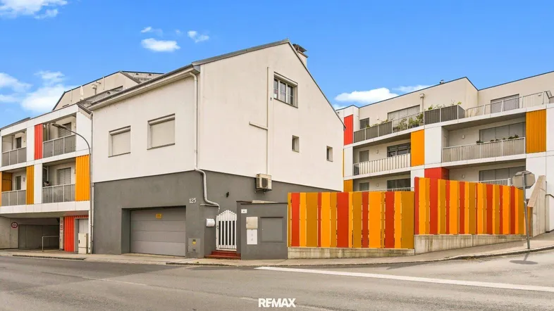 Moderne Wohngebäude mit farbigen Balkonfronten und integrierter Garage an einer Straße.
