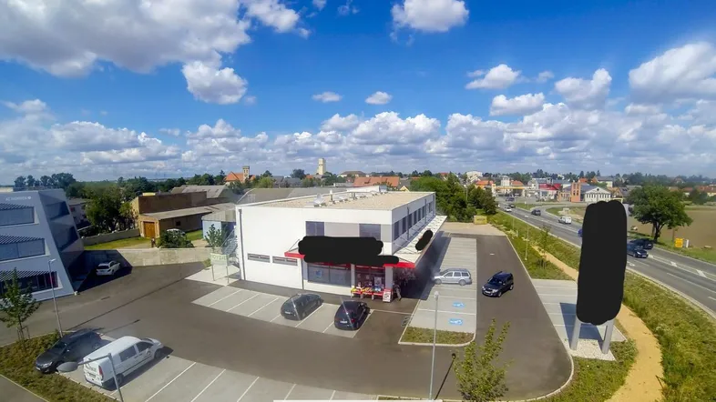 Luftaufnahme eines modernen Geschäftsgebäudes mit großem Parkplatz unter blauem Himmel und grüner Umgebung.