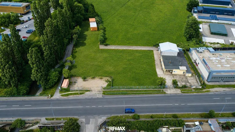 Luftaufnahme eines großen Grundstücks mit angrenzender Straße und umliegenden Gewerbegebäuden in grüner Umgebung.