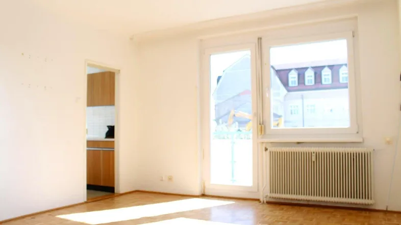 Helles Wohnzimmer mit Parkettboden, großen Fenstern und Zugang zu einem möglichen Außenbereich.